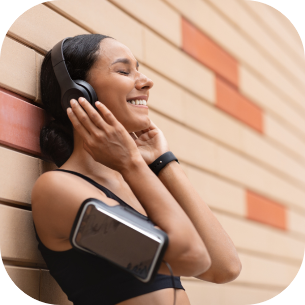 Woman leaning on wall listening to workout music with headphones and a phone in an fitness arm band rounded corners