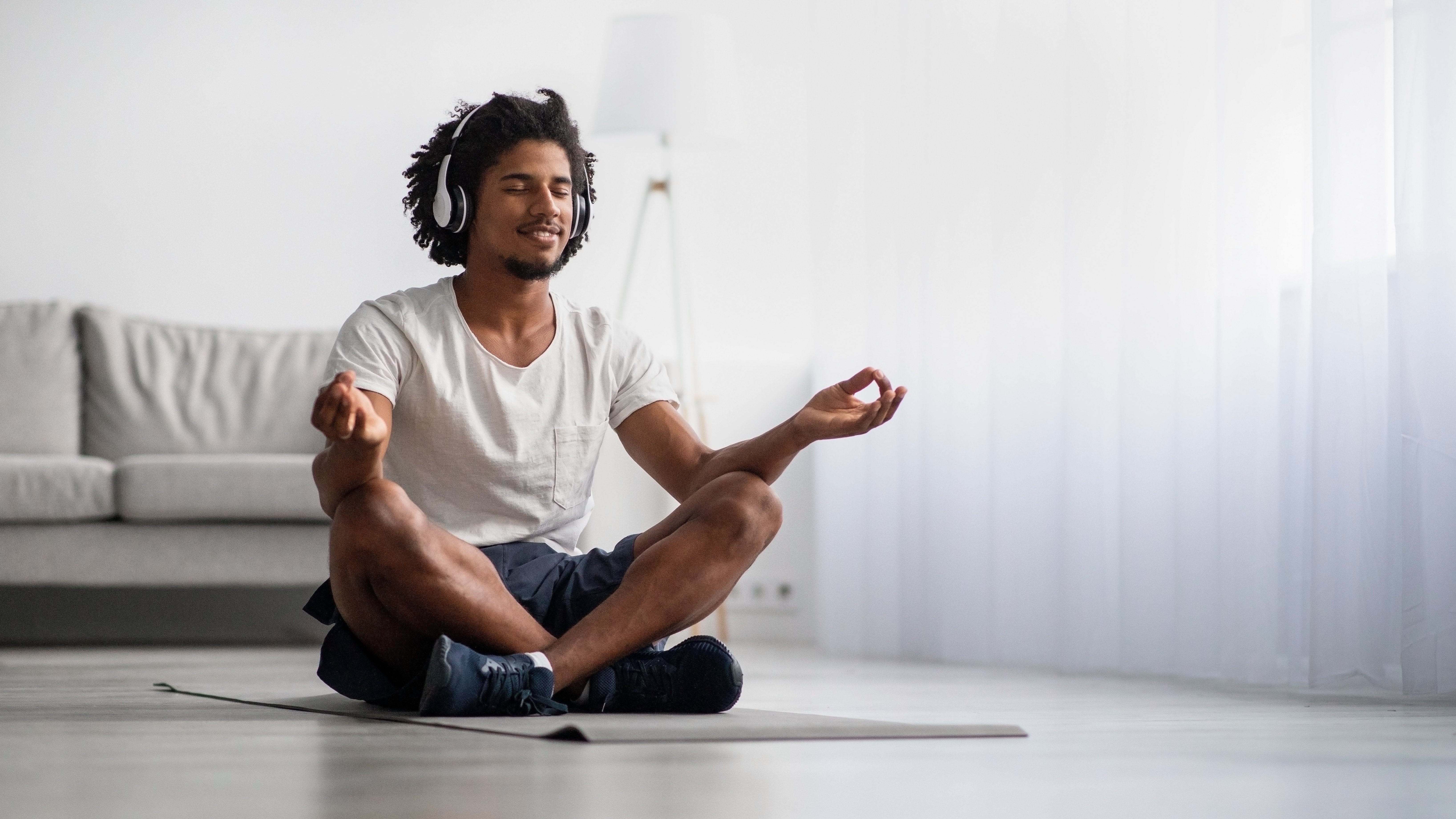 man meditating in yoga pose listening to wellness music with headphones