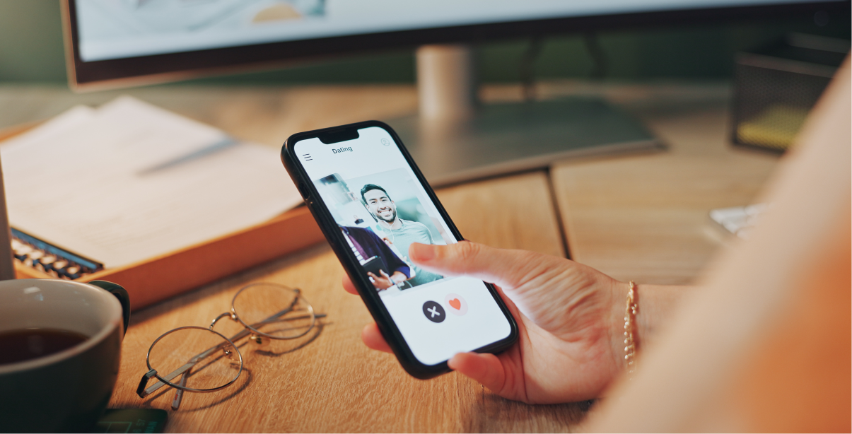 A person holding a smartphone displaying a dating app profile, swiping through matches on a mobile dating platform.