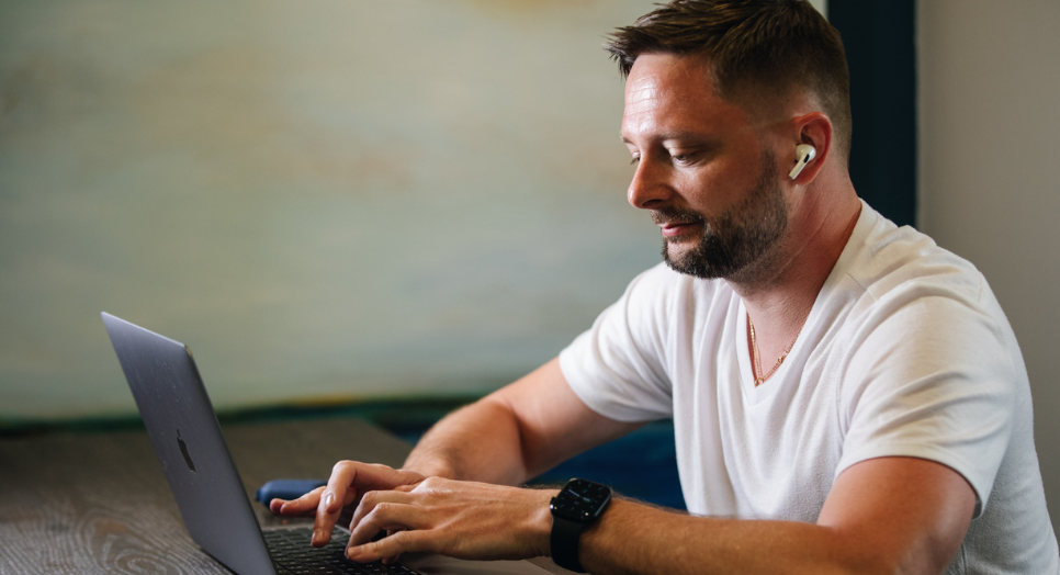 Mikhail, a developer at Feed Media Group, working on his laptop while wearing wireless earbuds, focused on coding and development tasks.