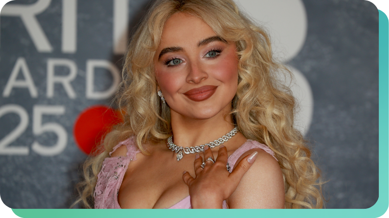 Sabrina Carpenter at an awards event, wearing a pink dress and diamond necklace, blonde curly hair