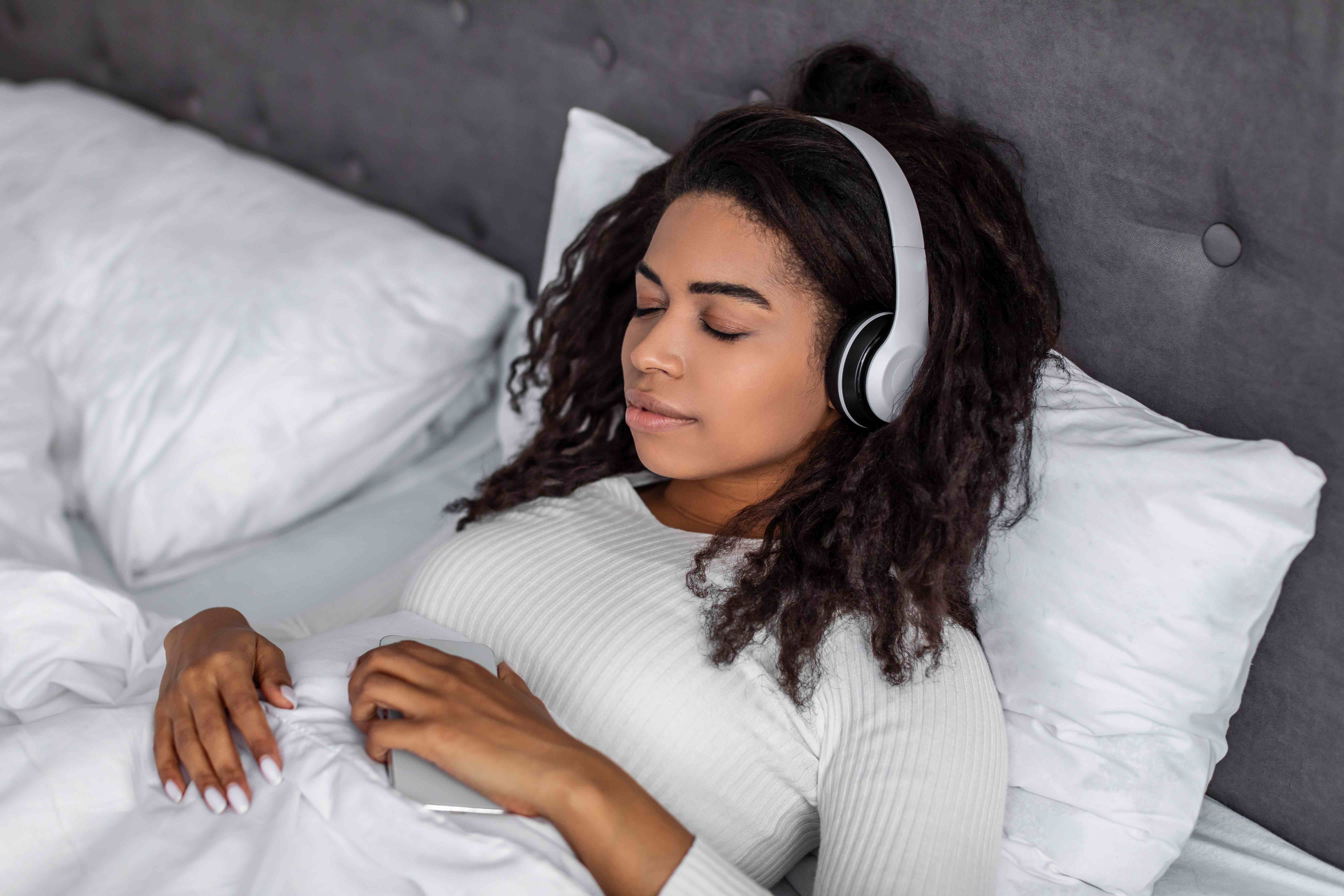 woman in bed listening to feed.fm music with headphones