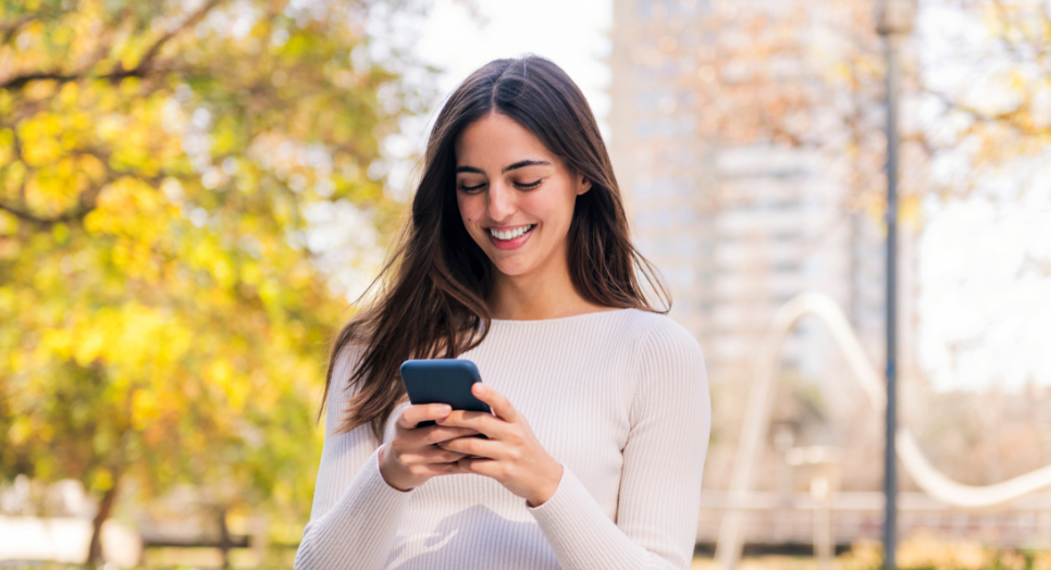 Woman smiling at phone outdoors personalized music experience on mobile.