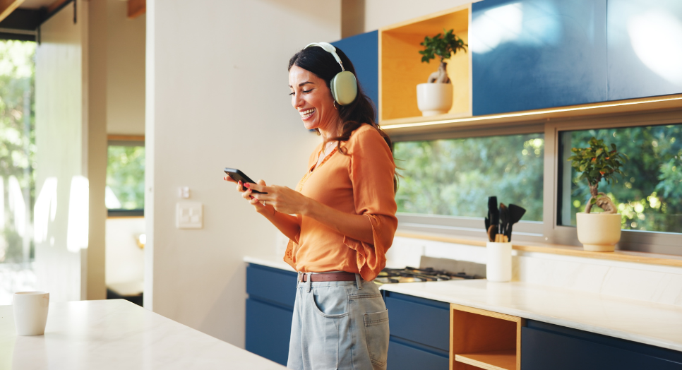 a woman on her phone wearing a orange top with jeans and headphones while listening to music